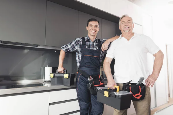 To mænd af blikkenslagere står i køkkenet og udgør med sorte værktøjskasser . - Stock-foto