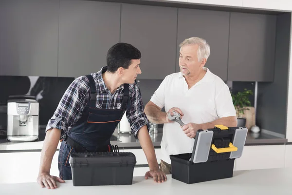 Dos hombres de fontaneros se paran en la cocina y eligen una herramienta para trabajar con tuberías que se fijan en el apartamento . —  Fotos de Stock