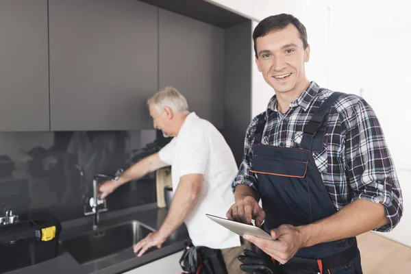 两个水管工人站在厨房里。一个老人检查修理工作的地方. — 图库照片