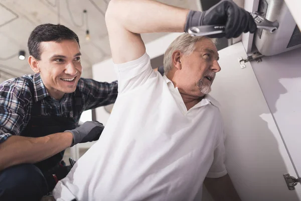 Two plumbers prepared to repair the kitchen sink. One of them is near the pipes, puts on gloves and preparing to help. — Stock Photo, Image