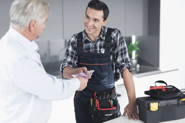 A plumber man communicates with a client who pays for the work done. The old man gives the plumber a fee. — Stock Photo, Image