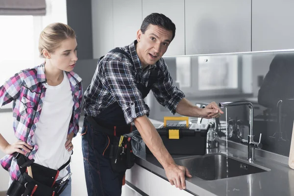 Um homem e uma mulher encanador reparar uma torneira de cozinha do cliente em casa . — Fotografia de Stock