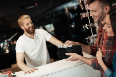 A man gives money to another man. They are in the store. The buyer has wallet with cash in his hand.