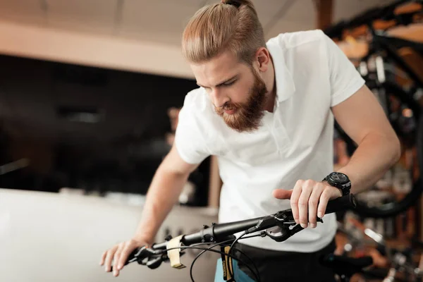 Un jeune homme barbu regarde les détails de la bicyclette dans le magasin de vélos . — Photo