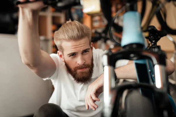 Ein junger Mann mit Bart betrachtet die Details des Fahrrads im Fahrradgeschäft. — Stockfoto