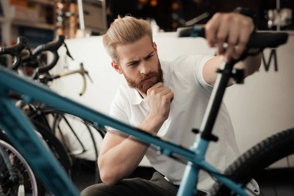 Молодой человек с бородой рассматривает детали велосипеда в магазине велосипедов . — стоковое фото