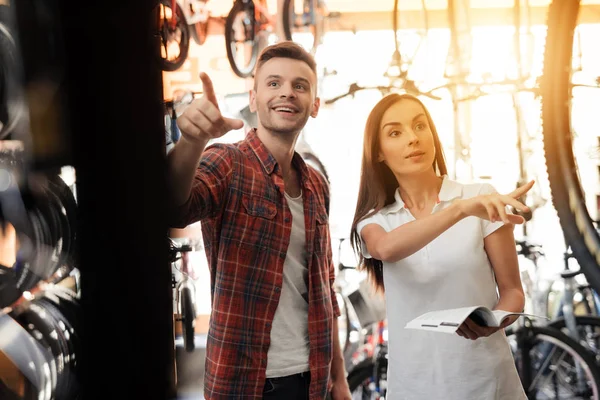 Una chica consultora muestra al comprador en una tienda de bicicletas . — Foto de Stock