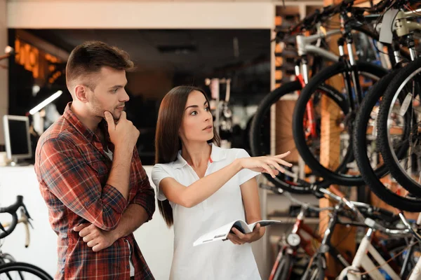 Una chica consultora muestra al comprador en una tienda de bicicletas . — Foto de Stock