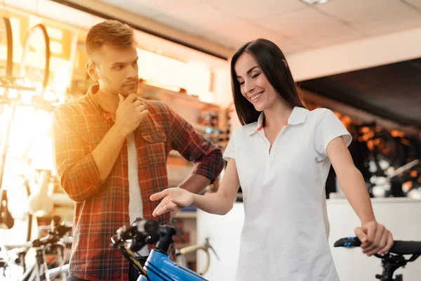 Una chica consultora muestra al comprador en una tienda de bicicletas . — Foto de Stock