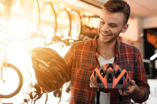 Ein junger Mann nimmt die Fahrradhelme unter die Lupe. — Stockfoto