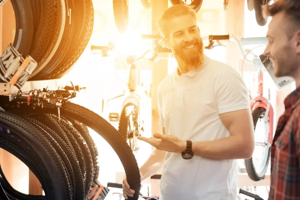 Un venditore in un negozio di biciclette aiuta un giovane acquirente a scegliere pneumatici per una bicicletta . — Foto Stock