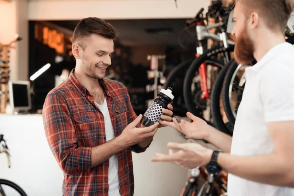 Un vendeur dans un magasin de vélos aide un jeune acheteur à choisir une bouteille d'eau pour des promenades à vélo . — Photo