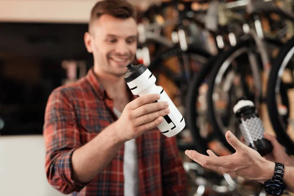 Verkäufer im Fahrradgeschäft hilft jungen Käufern bei der Auswahl einer Wasserflasche für Fahrradtouren. — Stockfoto