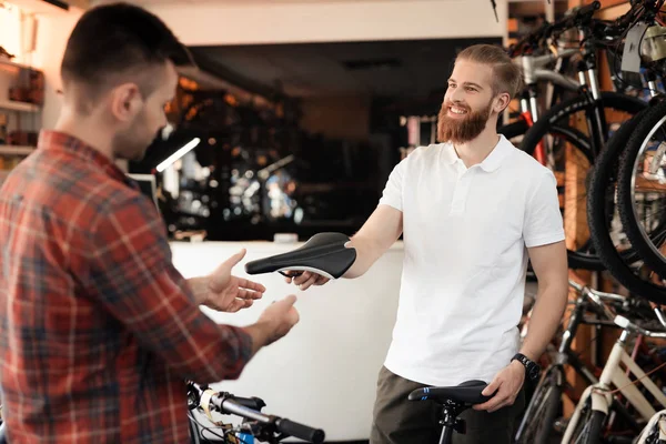 Verkäufer im Fahrradgeschäft hilft jungen Käufern bei der Wahl eines Sattels für ein Fahrrad. — Stockfoto