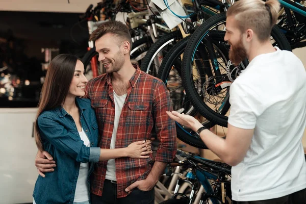 Un jeune homme barbu montre à un homme et à une femme une roue d'un vélo dans un magasin de vélos . — Photo