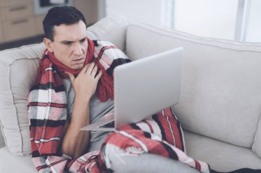 Soğuk bir adam kanepede, kırmızı halı saklanıyor oturuyor. O onun laptop ile kucağında oturuyor