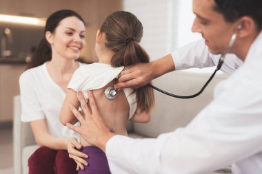 Küçük kız üşütmüş. Annesi evde doktor aradı. Doktor bir kıza bir stetoskop ile dinler.