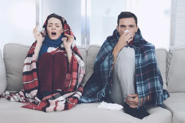 The couple is sitting on the couch wrapped in blankets. Man and woman are sick. The man flies out. Woman sneezing — Stock Photo, Image