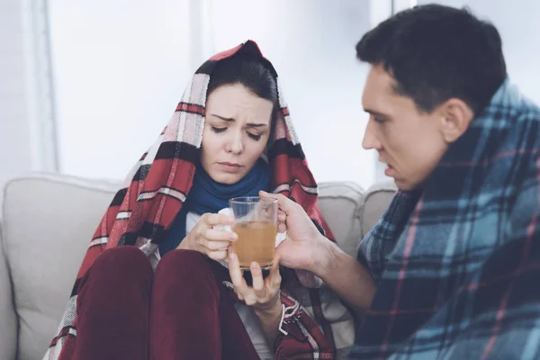 Çift battaniyelere sarılmış kanepede oturuyor. Erkek ve kadın hasta. Bir adam bir kadına şifalı çay verir. — Stok fotoğraf