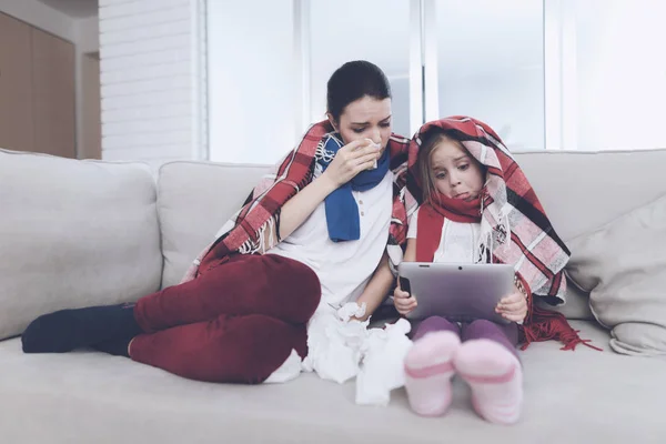 Жінка та її донька хворіють. вони сидять на дивані, загорнутому в ковдру — стокове фото