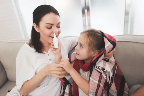 Девочка простудилась. Ее мать лечит ее. Девочка брызгает матери в нос носовым спреем. — стоковое фото