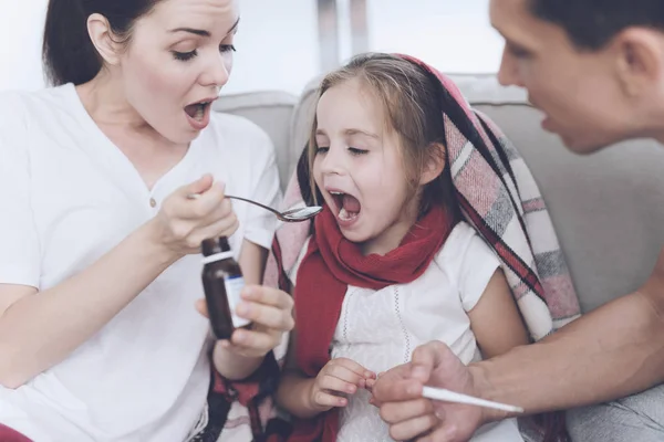 A menina apanhou uma constipação. A mãe e o pai estão a tratá-la. Mãe derrama um xarope de menina em uma colher — Fotografia de Stock