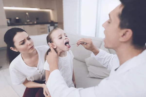 La niña se resfrió. Su madre llamó al médico en casa. El doctor mira la garganta de la chica. — Foto de Stock