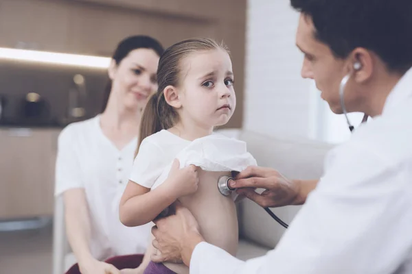 Das kleine Mädchen erkältete sich. Ihre Mutter rief den Arzt zu Hause an. Arzt hört einem Mädchen mit Stethoskop zu — Stockfoto