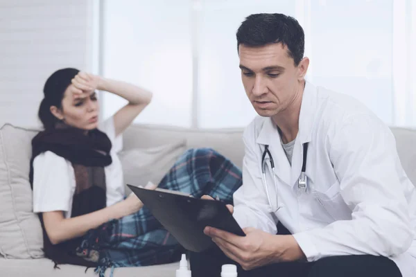 Wanita itu jatuh sakit dan menelepon dokter di rumah. Dia duduk di sofa dengan selimut. Dokter duduk di dekat sini — Stok Foto