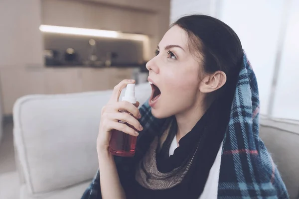 A cold woman sits on a light couch wrapped in a blue checkered whip. She sits plaid over her head — Stock Photo, Image