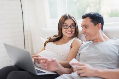 Hamile bir kadın ve bir adam yatakta yatıyordu. Bir kadın bir dizüstü bilgisayar onun kucağına tutuyor, bir adam bir smartphone tutuyor.