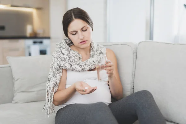 Sjuka gravid kvinna sitter hemma i soffan. Hon redo att dricka ett piller. — Stockfoto