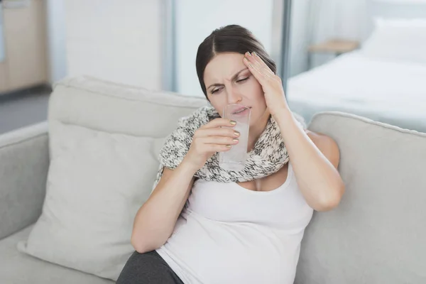 Malade femme enceinte assise à la maison sur le canapé. Elle boit un comprimé dissous dans l'eau — Photo