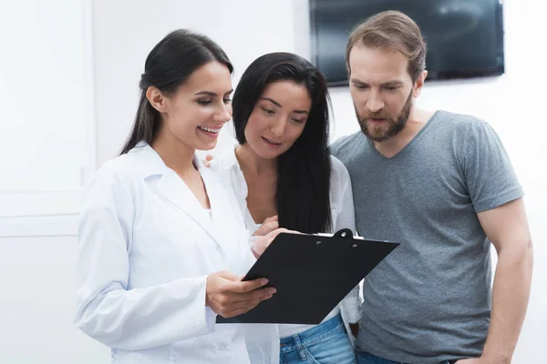 Un homme et une femme sont venus voir un dentiste. Ils ont été accueillis par la réceptionniste, il leur montre les informations sur le formulaire . — Photo