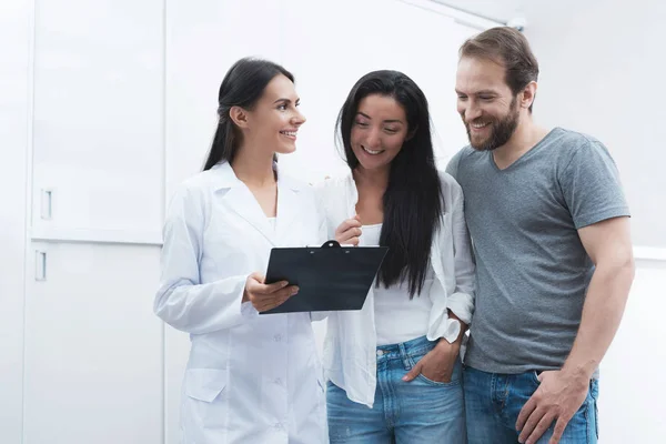 Un homme et une femme sont venus voir un dentiste. Ils ont été accueillis par la réceptionniste, il leur montre les informations sur le formulaire . — Photo