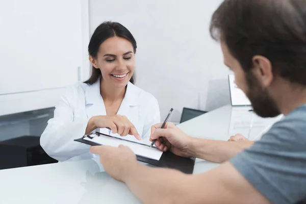 Tajemník v lékařské kliniky pomáhá pacientovi vyplnit potřebné formuláře před zahájením léčby. — Stock fotografie