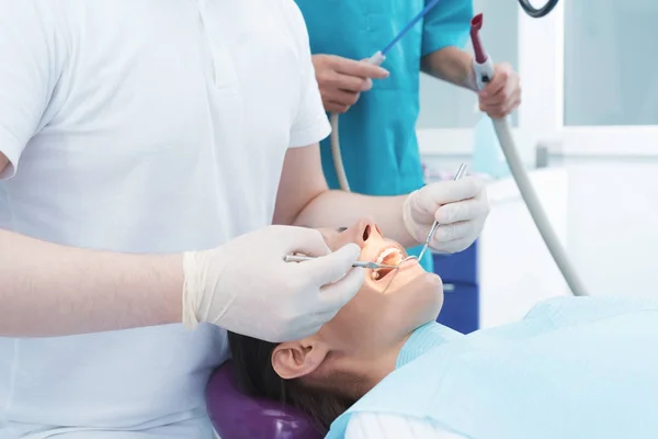 Una mujer está sentada en una silla dental en la recepción de un dentista. Un médico masculino está tratando los dientes del paciente. . — Foto de Stock
