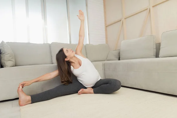 Hamile bir kadın evde hafif bir katta oturuyor. Yoga egzersizleri yapıyor — Stok fotoğraf