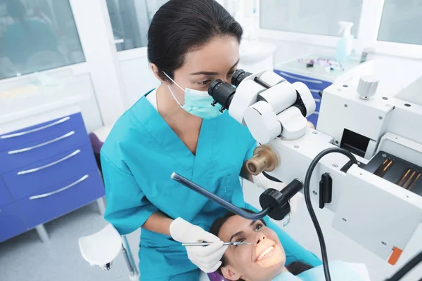 A female dentist is treating a patient. She is sitting on the dental chair. The doctor uses a special dental instrument. — Stock Photo, Image