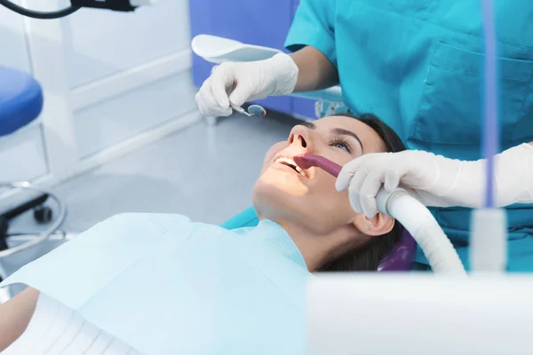 Kobieta dentysty jest traktowanie pacjenta. Ona siedzi na Fotel dentystyczny. Lekarz używa specjalnego instrumentu stomatologiczne. — Zdjęcie stockowe