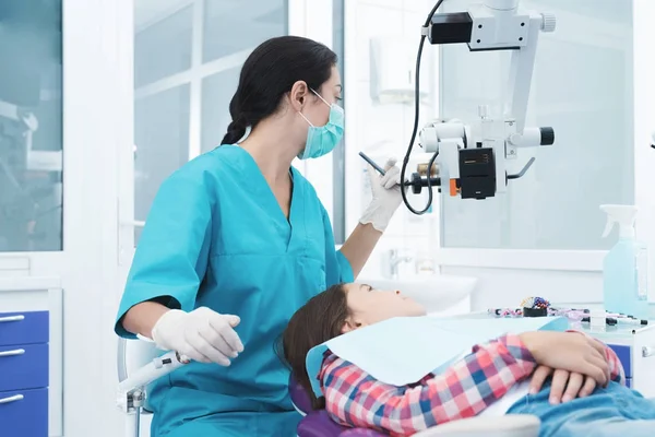 Uma dentista está a tratar uma rapariga. Ela senta-se na cadeira dentária e sorri . — Fotografia de Stock