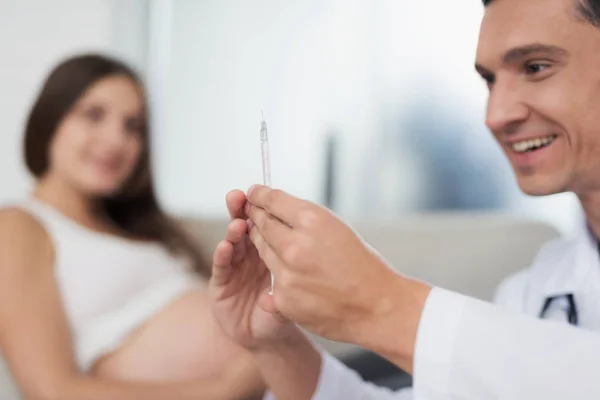 Een zwangere vrouw ligt op een lichte sofa thuis. Een dokter kwam om haar, hij bereidt een spuit voor de injectie. — Stockfoto