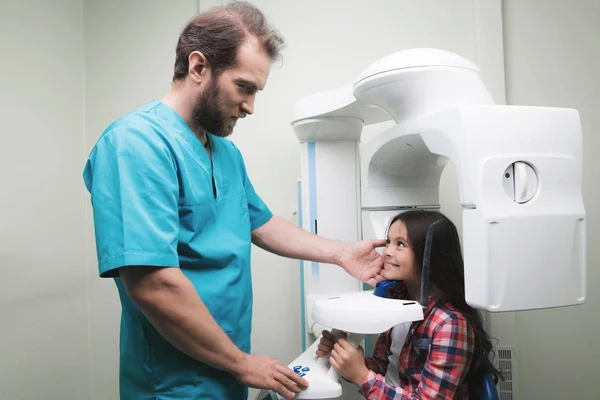 Ein Arzt macht ein Röntgenbild des Kiefers des Mädchens, das in einem speziellen Röntgengerät sitzt. das Mädchen lächelt. — Stockfoto