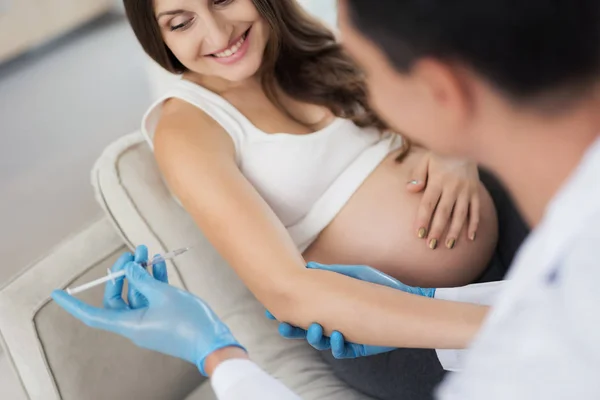 Uma mulher grávida está deitada em um sofá leve em casa. Um médico veio ter com ela, ele faz uma injecção de mulher no braço — Fotografia de Stock