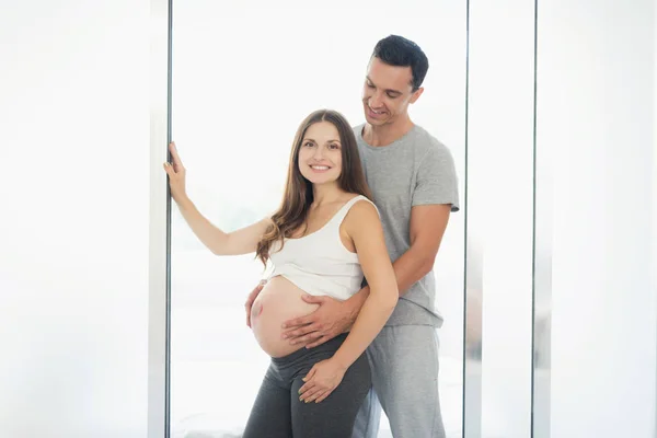 Eine schwangere Frau posiert mit ihrem Mann. Er umarmt sie von hinten. Sie hat ein Herz auf dem Bauch — Stockfoto