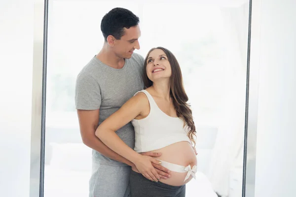 Schwangere zu Hause. sie hat eine weiße Schleife auf dem Bauch — Stockfoto