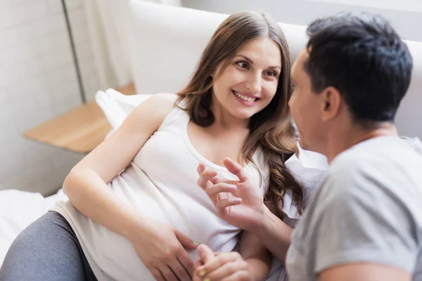 妊娠中の女性と男性は、ベッドに横たわっています。彼らは何かについて話す — ストック写真