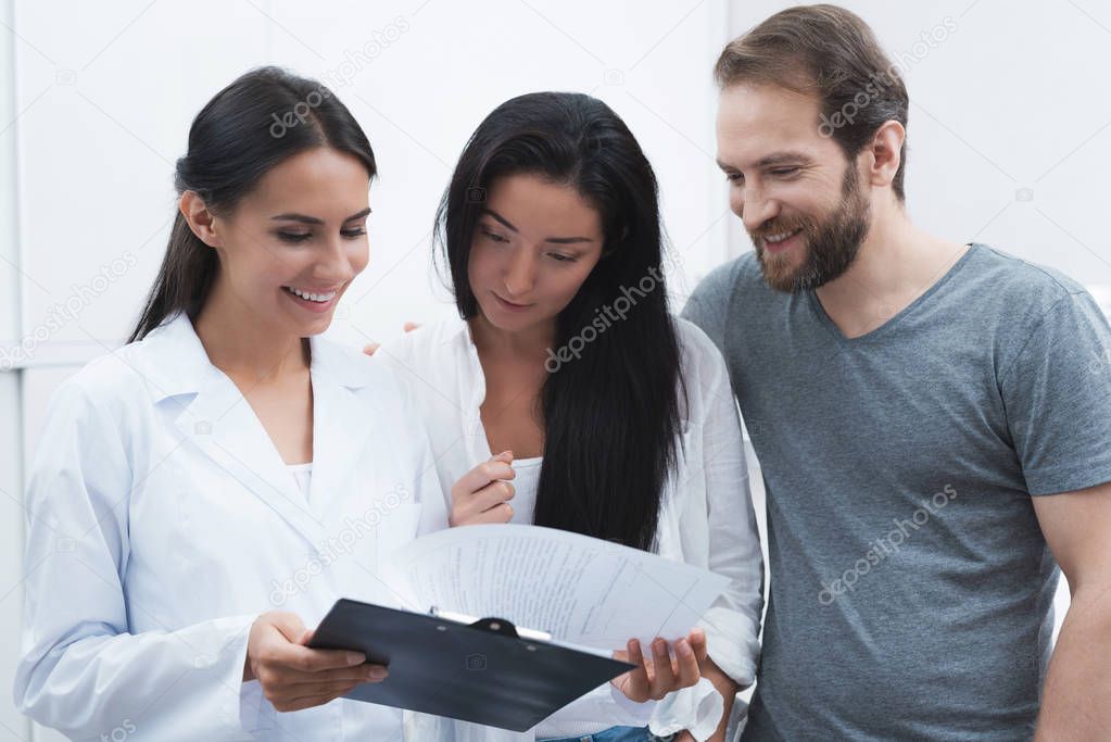 A man and a woman came to see a dentist. They were met by the receptionist, he shows them the information on the form.