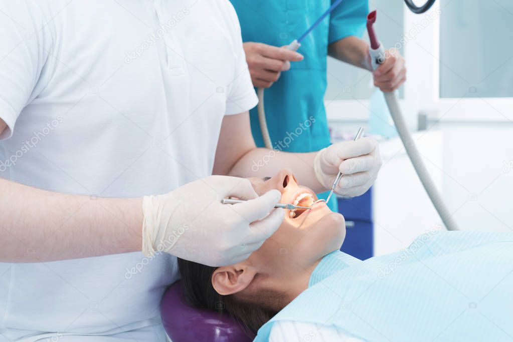 A woman is sitting in a dental chair at a dentist's reception. A male doctor is treating the patient teeth.