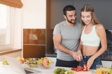 Bir çift bir salata kahvaltı için hazırlanıyor. Bir kız için bir salata sebze keser ve bir adam ona yardımcı olur.